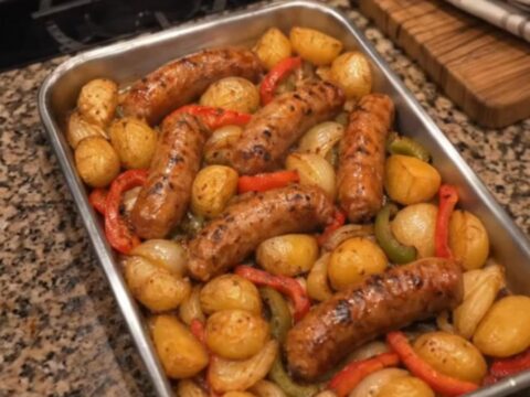 A sizzling sheet pan of roasted sausage chunks, crispy golden baby potatoes, and charred peppers