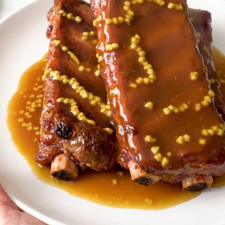 A plate of glossy, golden-brown honey mustard country-style ribs served on a clean white plate.