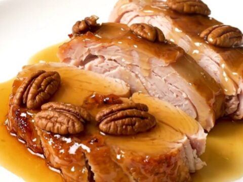 A close-up of sliced maple pecan turkey tenderloin medallions with a glossy glaze on a white plate.