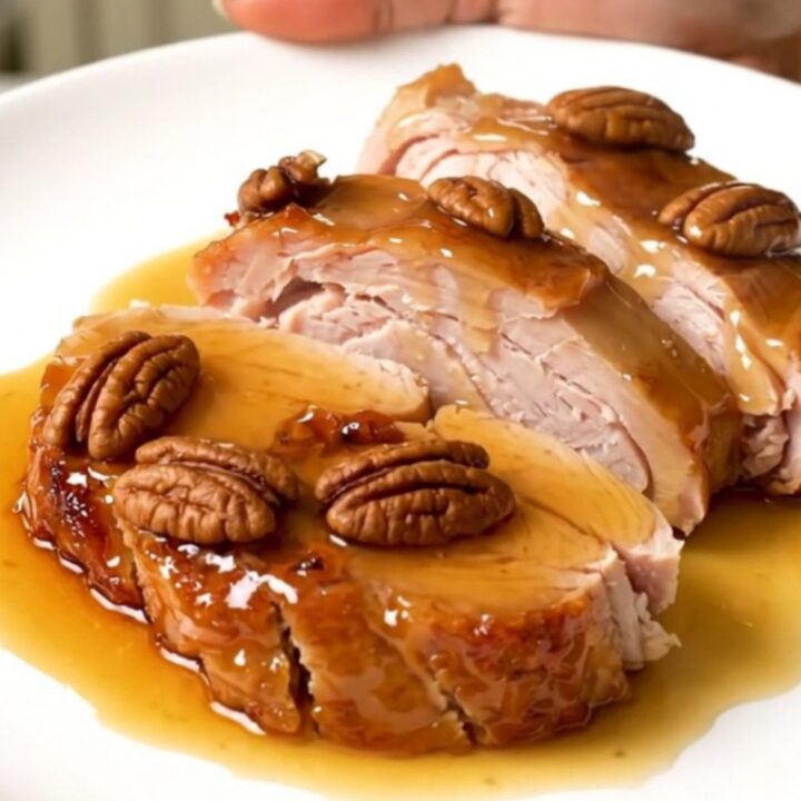 A close-up of sliced maple pecan turkey tenderloin medallions with a glossy glaze on a white plate.