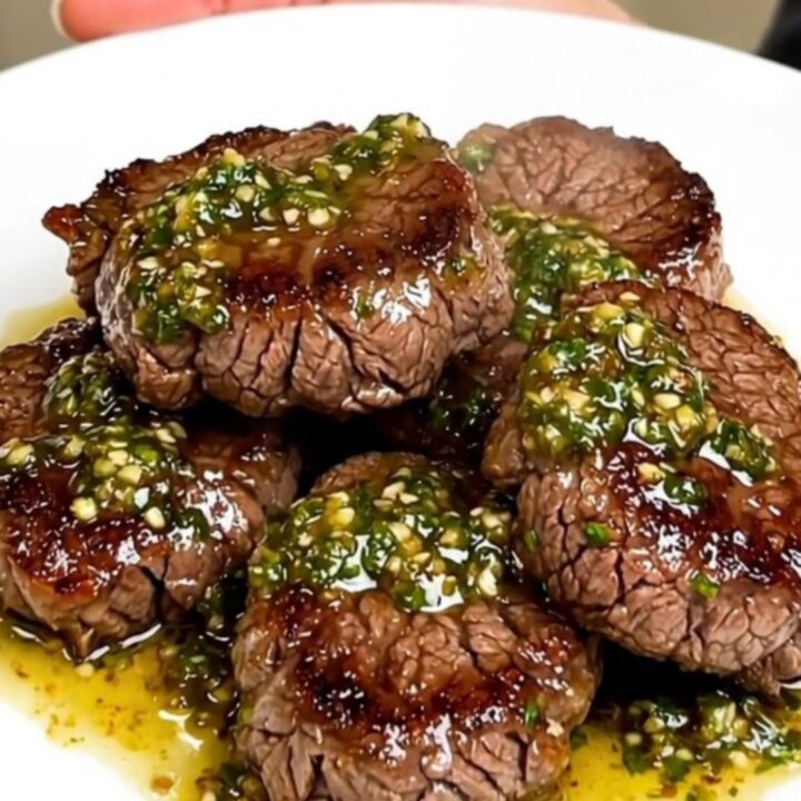 A close-up of tender, glossy chimichurri steak bites served on a plain white plate.