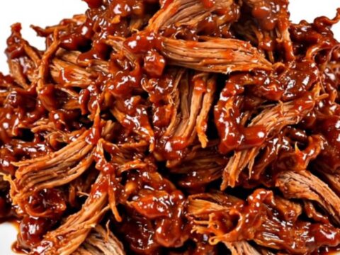 A white plate topped with a generous portion of glossy, shredded Korean-style pork with visible steam rising from it.