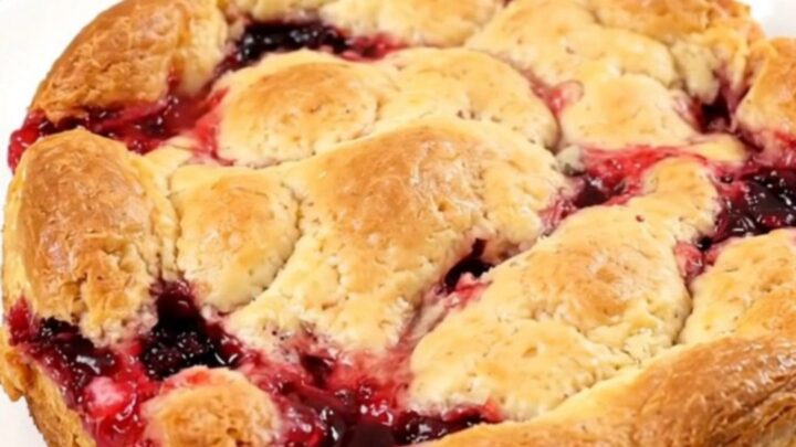 A top-down view of a black oval slow cooker filled with a bubbling apple and berry cobbler, topped with melted butter.