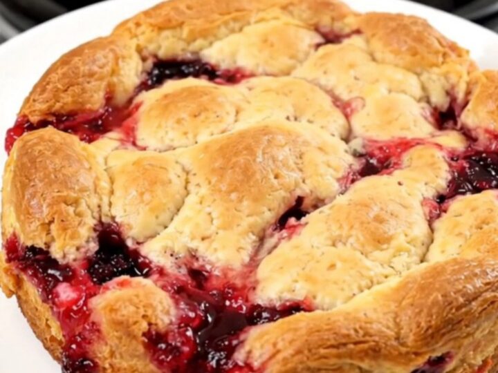 A top-down view of a black oval slow cooker filled with a bubbling apple and berry cobbler, topped with melted butter.