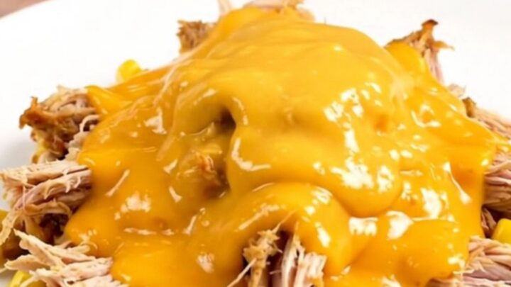 A top-down view of a slow cooker filled with raw chicken breasts, corn, ranch seasoning, and cheddar soup.