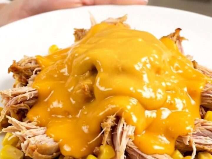 A top-down view of a slow cooker filled with raw chicken breasts, corn, ranch seasoning, and cheddar soup.