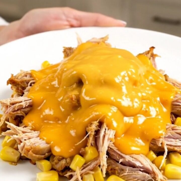 A top-down view of a slow cooker filled with raw chicken breasts, corn, ranch seasoning, and cheddar soup.