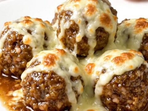 A slow cooker filled with beef meatballs, French onion soup, and melted provolone cheese on a white countertop.