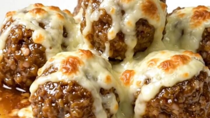 A slow cooker filled with beef meatballs, French onion soup, and melted provolone cheese on a white countertop.