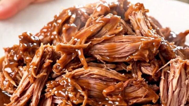 A close-up view of juicy, shredded chipotle lime pulled pork served on a white plate.