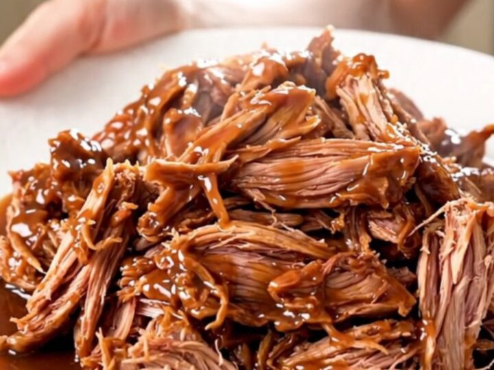 A close-up view of juicy, shredded chipotle lime pulled pork served on a white plate.