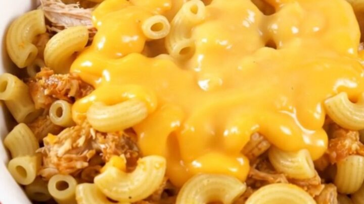 A steaming bowl of cheesy taco macaroni with shredded chicken served in a white bowl.