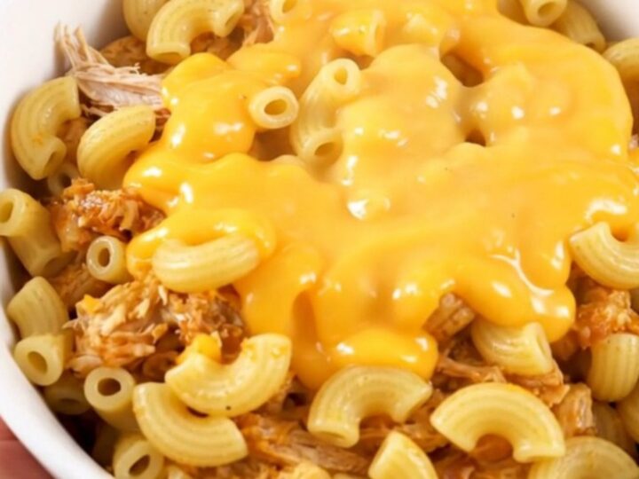 A steaming bowl of cheesy taco macaroni with shredded chicken served in a white bowl.