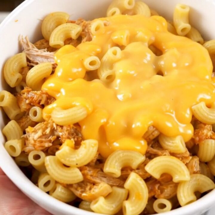 A steaming bowl of cheesy taco macaroni with shredded chicken served in a white bowl.