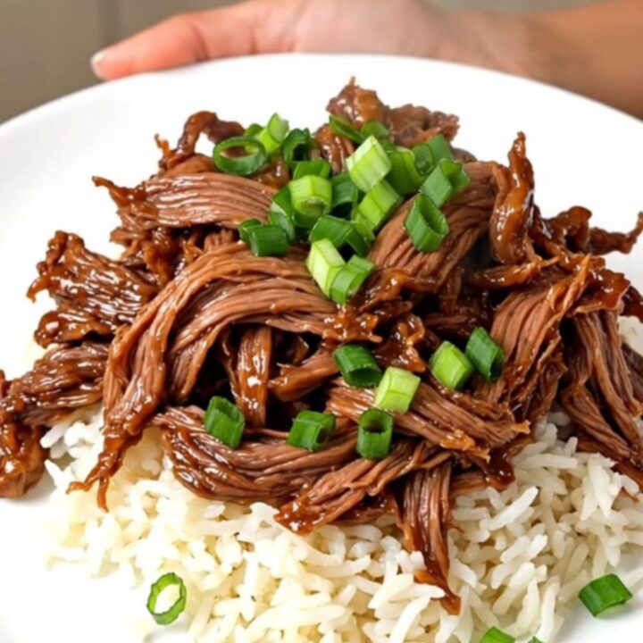 A close-up view of tender, glossy teriyaki shredded beef served over white jasmine rice with scallion garnish.