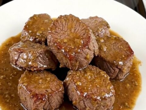 A close-up view of tender, glistening slow-cooked steak bites and mushrooms served on a clean white plate.