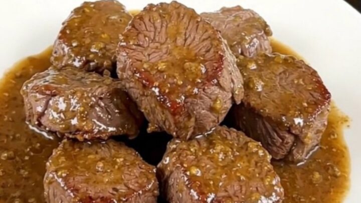 A close-up view of tender, glistening slow-cooked steak bites and mushrooms served on a clean white plate.