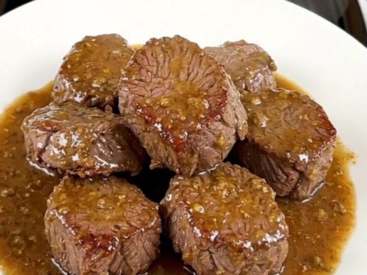 A close-up view of tender, glistening slow-cooked steak bites and mushrooms served on a clean white plate.