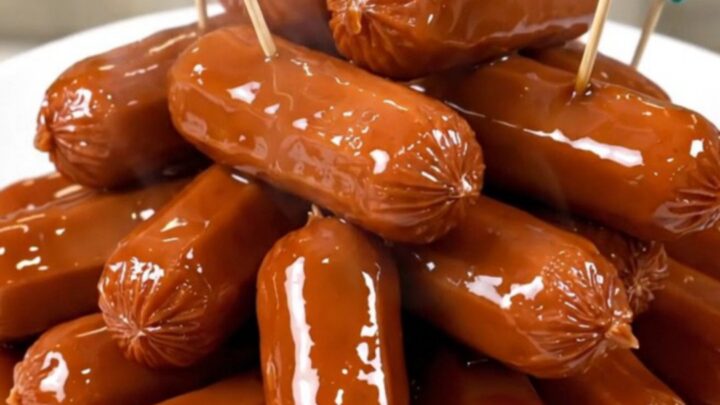 A close-up of glossy, dark brown cocktail smokies in a slow cooker with pineapple tidbits.