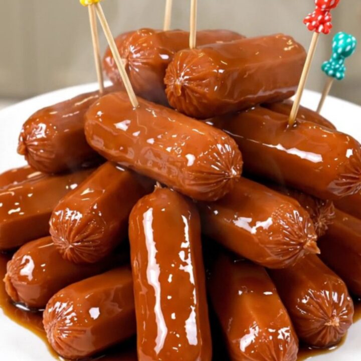 A close-up of glossy, dark brown cocktail smokies in a slow cooker with pineapple tidbits.