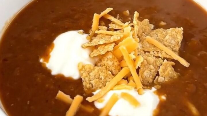 A steaming bowl of ground beef enchilada soup topped with sour cream, shredded cheese, and tortilla chips.