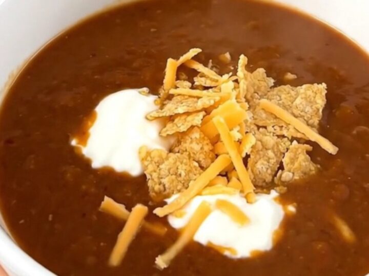 A steaming bowl of ground beef enchilada soup topped with sour cream, shredded cheese, and tortilla chips.