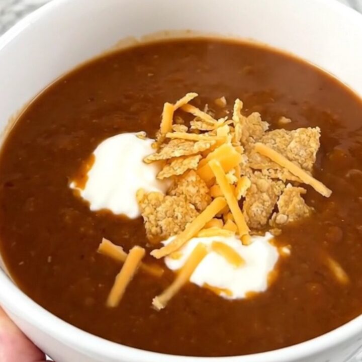 A steaming bowl of ground beef enchilada soup topped with sour cream, shredded cheese, and tortilla chips.