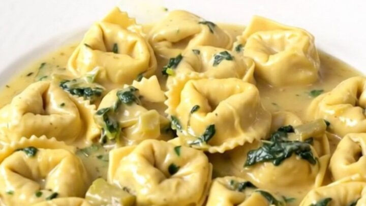 A steaming, creamy slow cooker spinach artichoke tortellini bake in a black ceramic insert.