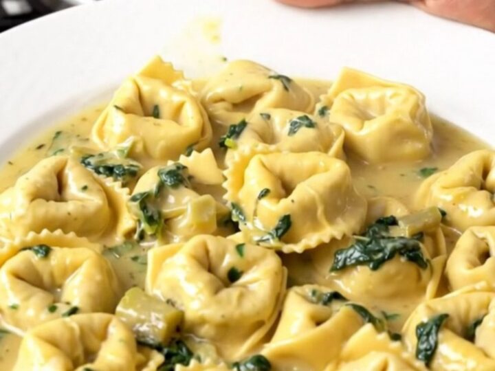 A steaming, creamy slow cooker spinach artichoke tortellini bake in a black ceramic insert.