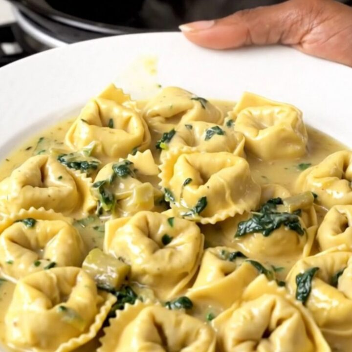 A steaming, creamy slow cooker spinach artichoke tortellini bake in a black ceramic insert.