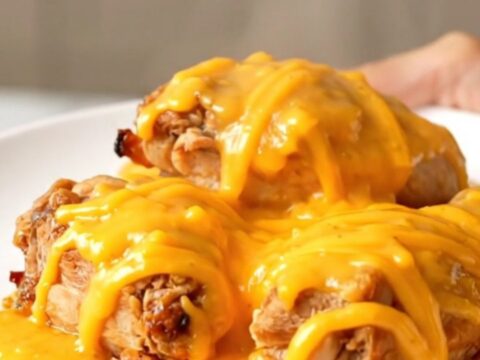 A close-up view of the finished slow cooker honey mustard chicken topped with melted sharp cheddar cheese on a white plate.
