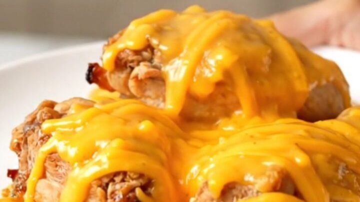 A close-up view of the finished slow cooker honey mustard chicken topped with melted sharp cheddar cheese on a white plate.