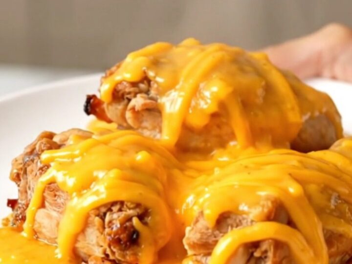 A close-up view of the finished slow cooker honey mustard chicken topped with melted sharp cheddar cheese on a white plate.