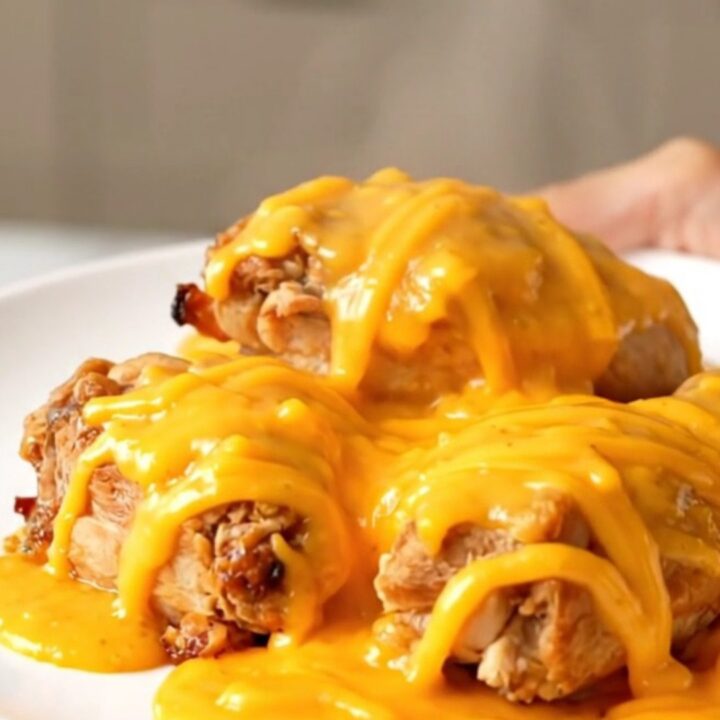A close-up view of the finished slow cooker honey mustard chicken topped with melted sharp cheddar cheese on a white plate.