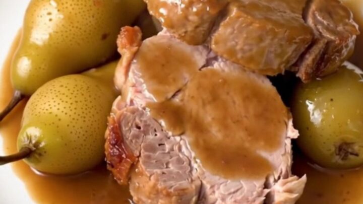 Sliced pork tenderloin served on a white plate with glazed pears and a light sauce.