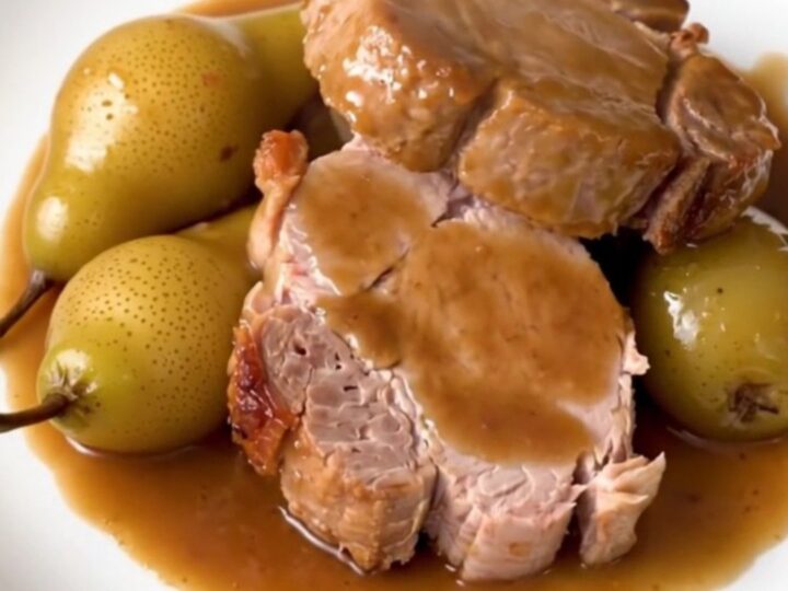Sliced pork tenderloin served on a white plate with glazed pears and a light sauce.