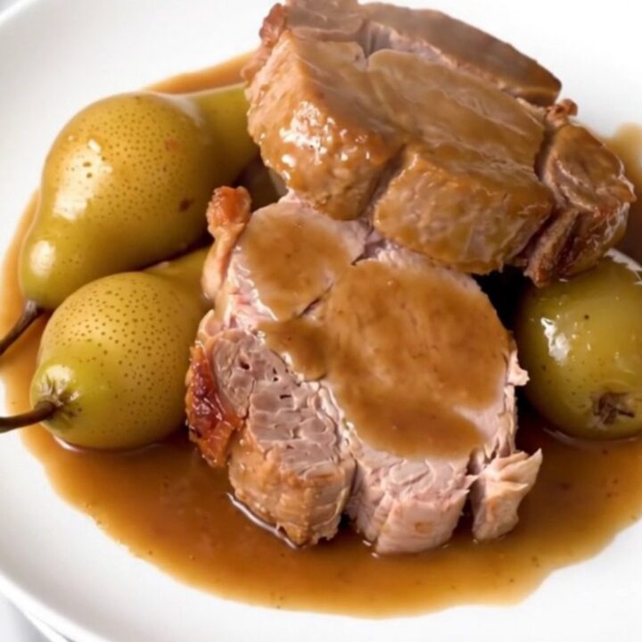 Sliced pork tenderloin served on a white plate with glazed pears and a light sauce.