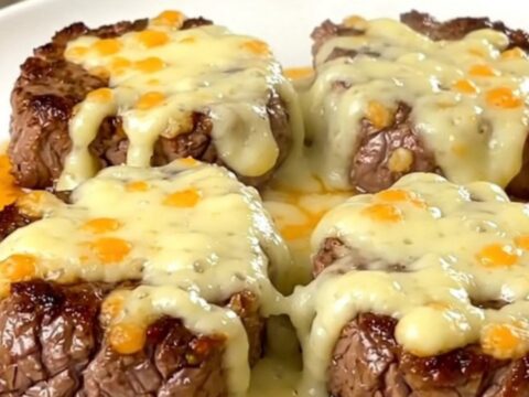 A plate of tender, slow-cooked steak bites coated in melted pepper jack cheese and green chiles.