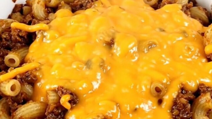 A bowl of steaming beef chili topped with melted cheddar cheese in a home kitchen setting.