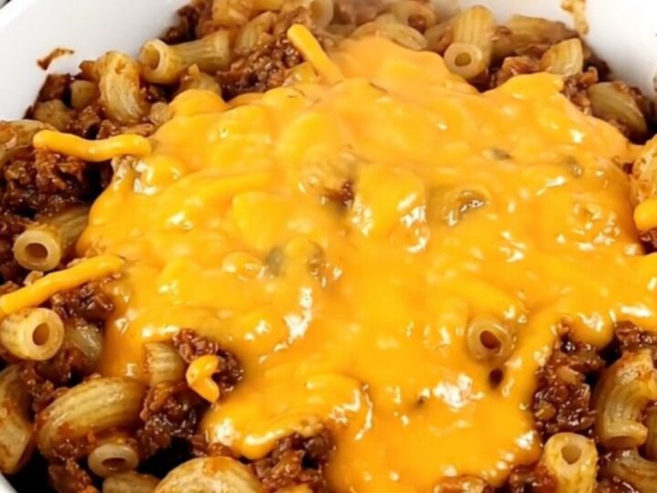 A bowl of steaming beef chili topped with melted cheddar cheese in a home kitchen setting.