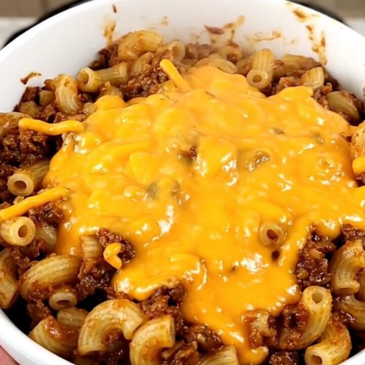 A bowl of steaming beef chili topped with melted cheddar cheese in a home kitchen setting.