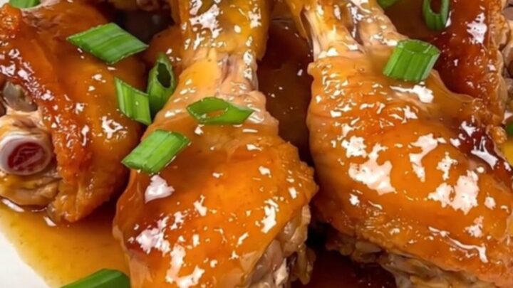 A close-up of glossy orange glazed chicken drumsticks on a white plate with green onions.