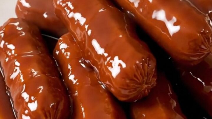 A top-down view of raw cocktail sausages, brown sugar, onion powder, and barbecue sauce in a slow cooker.