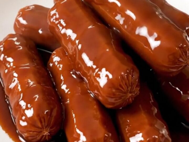 A top-down view of raw cocktail sausages, brown sugar, onion powder, and barbecue sauce in a slow cooker.