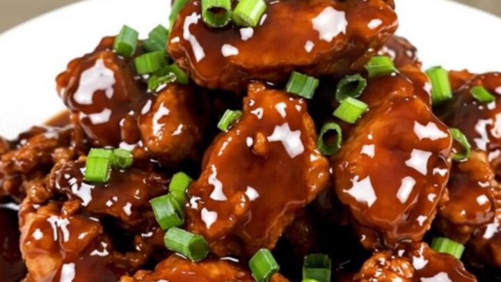 A plate of finished, glossy Mongolian chicken with green onions served on a white plate.