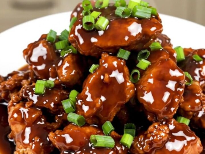 A plate of finished, glossy Mongolian chicken with green onions served on a white plate.