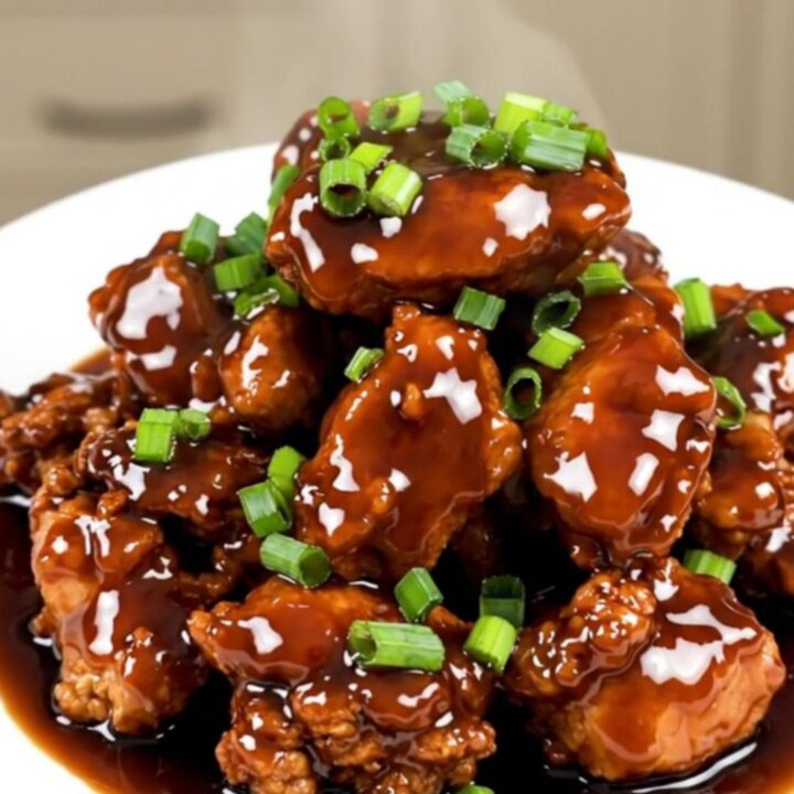 A plate of finished, glossy Mongolian chicken with green onions served on a white plate.