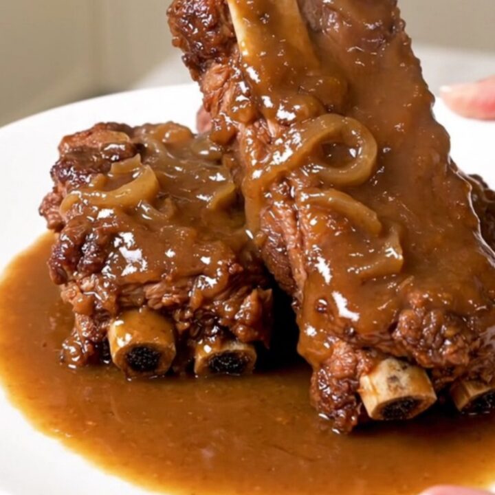 Slow-cooked country-style pork ribs covered in a rich, savory onion and mushroom gravy on a white plate.