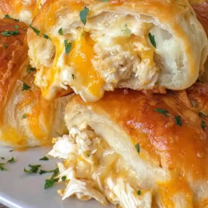 A close-up of flaky golden crescent rolls pulled apart to reveal steaming chicken and melted cheese