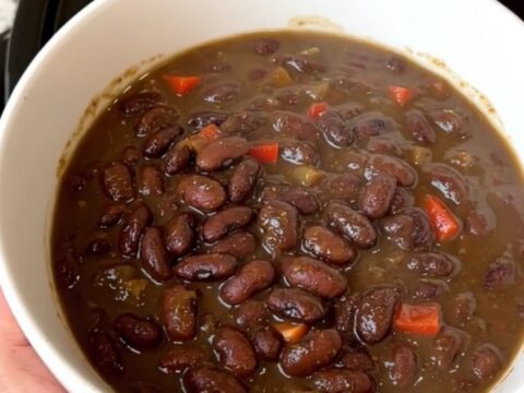A top-down view of a black slow cooker filled with black bean stew and colorful red bell peppers.